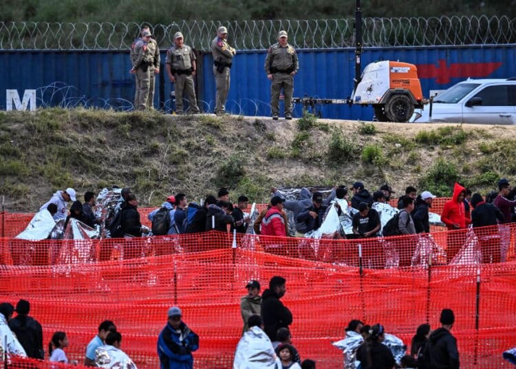 Customs and Border Protection agents stand guard as immigrants wait to be processed after illegally crossing the border from Mexico at Eagle Pass, Texas, on Dec. 22.