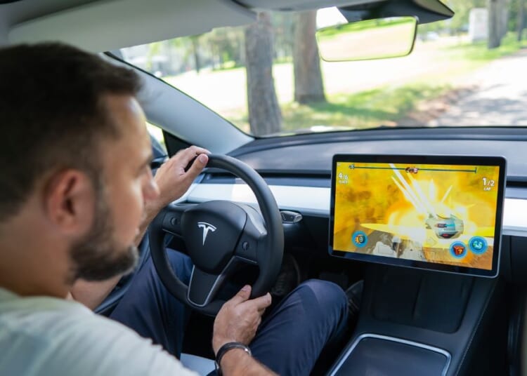 A man looks at the dashboard while driving a Tesla in this stock image.