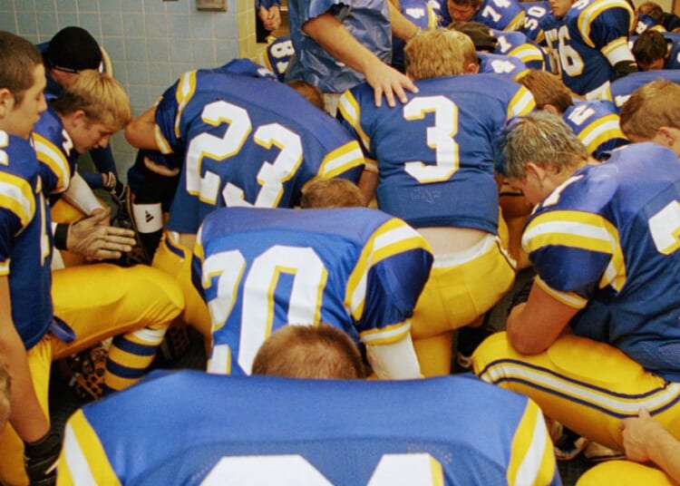 This stock image shows a high school football team praying before a game.